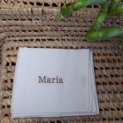Guardanapo branco com nome bordado Maria sobre superfície de rattan e bambu