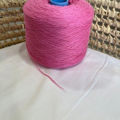 Rolo grande de linha rosa sobre tecido branco e fundo de fibras naturais