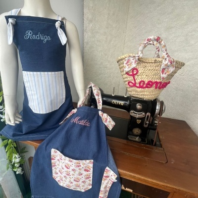Dois aventais azuis com nomes bordados e bolsa de palha com nome bordado