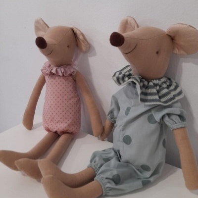 Dois bonecos de rato de tecido com roupas coloridas sentados sobre superfície branca