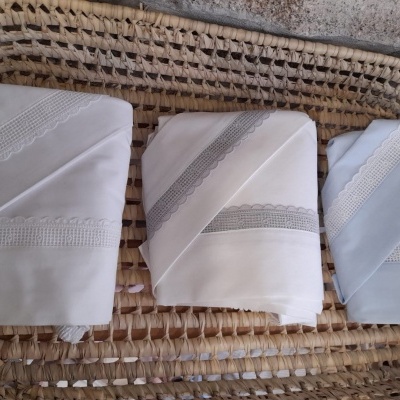 Três panos de tecido com rendas, em branco, creme e azul claro, sobre superfície entrelaçada.