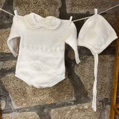 Conjunto de bebé em malha branca com body e gorro pendurados num estendal