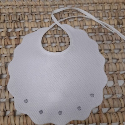 Babete branco com bordas onduladas e cinco pontos cinzentos sobre vime entrelaçado