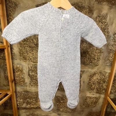 Macacão de bebé cinzento claro em malha pendurado num cabide de madeira