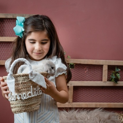 Menina segurando cesta de sisal com coelho branco em interior com parede rosa