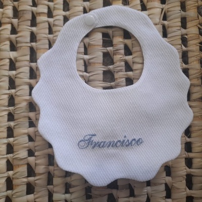 Babete branco bordado com nome Francisco, sobre tecido trançado castanho