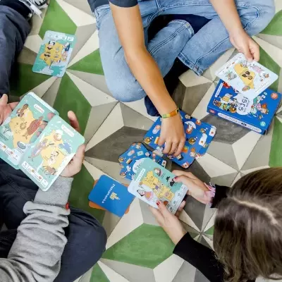 Crianças a jogar cartas coloridas sentadas em chão de azulejos geométricos