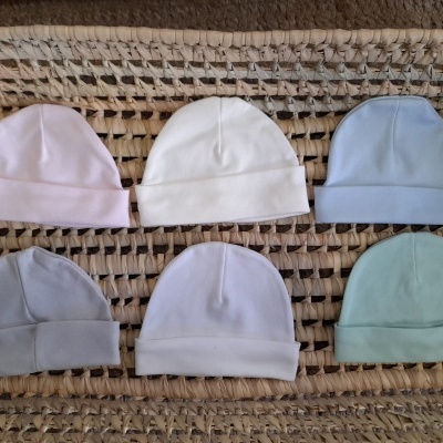 Seis gorros de bebê coloridos sobre superfície de fibra natural