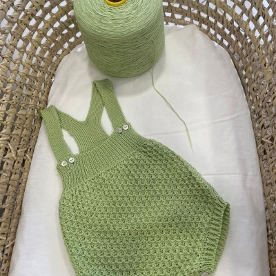 Roupa de bebé verde pistacho em malha com botões numa cesta de verga com fio ao lado.