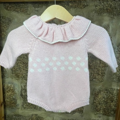 Body bebé rosa com bolinhas brancas e babado, pendurado num cabide de madeira