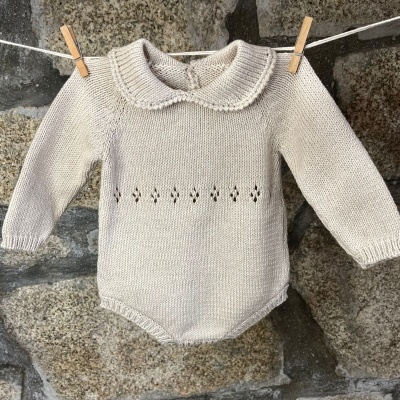 Body de bebé bege claro em malha com gola e pequenos buracos decorativos pendurado num estendal com molas de madeira