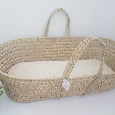 Moisés oval de palha natural com almofada branca e planta ao lado