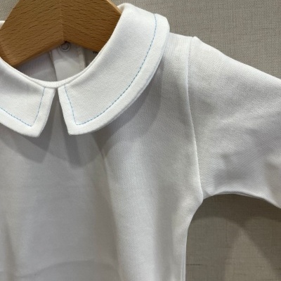 Roupa de bebé branca com gola redonda dupla e costura azul clara pendurada num cabide de madeira
