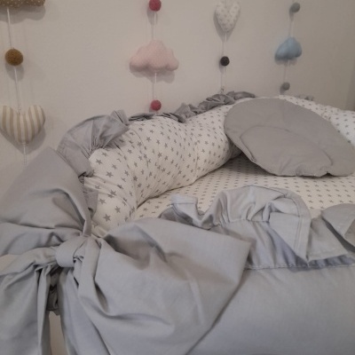 Berço de bebé cinzento com almofada redonda e decoração de parede em tecido de nuvens e corações coloridos