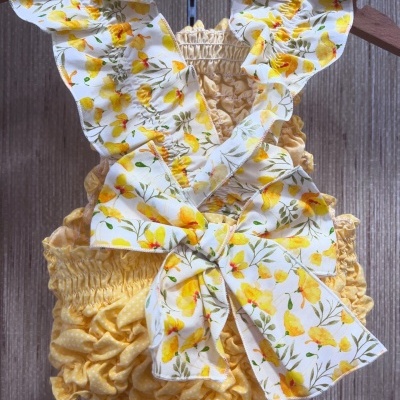 Roupa de bebé amarela com alças florais e laço grande
