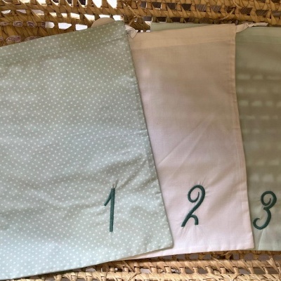 Três sacos têxteis coloridos numerados 1, 2 e 3 sobre cesta de vime