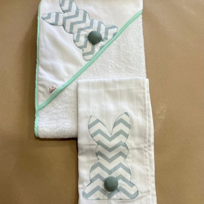 Toalha branca com borda verde and fralda branca com padrão de coelho cinzento com riscas em zig-zag