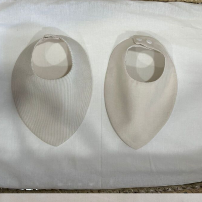 Dois babetes de bebé bege com fecho de botão de pressão sobre tecido branco