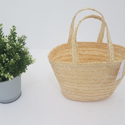 Cesto de palha natural com duas pegas ao lado de planta verde em vaso cinza