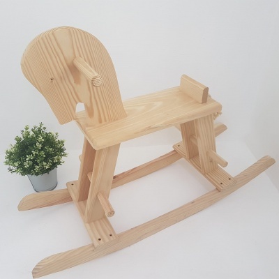 Cavalo baloiço em madeira clara com vaso de planta ao lado