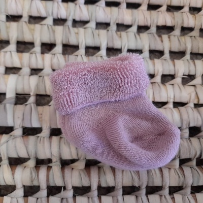 Meia infantil cor de rosa com punho felpudo sobre tapete de ráfia branco e preto