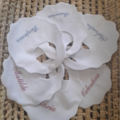 Seis toalhetes brancos bordados com nomes em várias cores sobre superfície trançada de palha