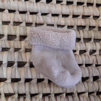 Meia de bebé cinza claro sobre superfície entrelaçada de fibras naturais