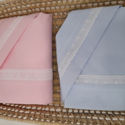 Lençóis de berço rosa e azul claro com renda branca numa cesta de vime
