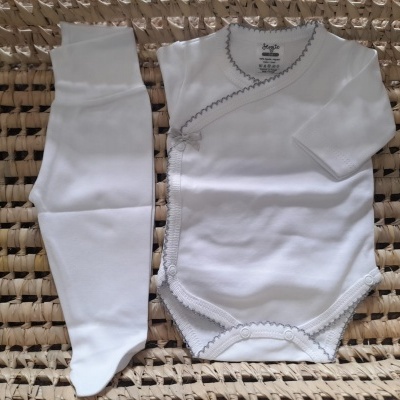 Conjunto de bebé branco com bordado cinza sobre cesto de vime