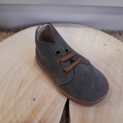 Sapatinho infantil de camurça cinzento com atacadores castanhos sobre madeira