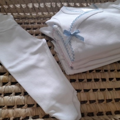 Roupas brancas de bebé com detalhes azuis e meia-calça branca em tecido trançado