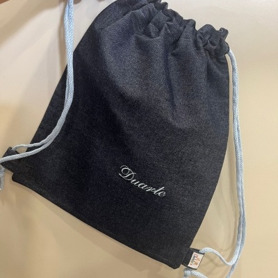Mochila saco cinzento escuro com cordões brancos e texto 'Duante'