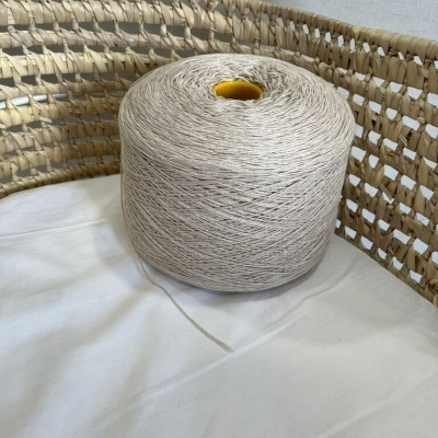 Cone de fio bege em tecido branco junto a cadeira trançada de palha