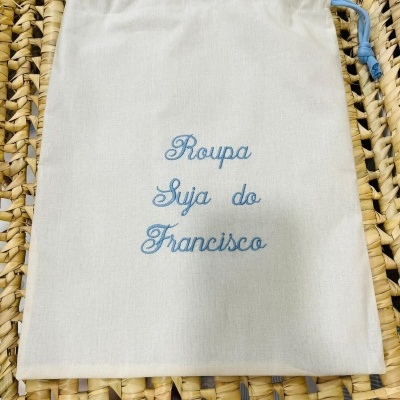 Saco branco com cordão azul e bordado azul sobre superfície de cestaria trançada