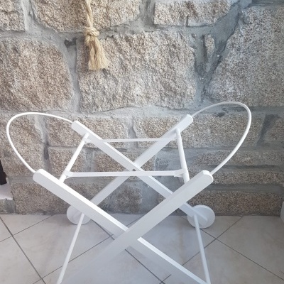 Suporte branco metálico com rodas para carrinho ou cesto, em chão de azulejo junto a parede de pedra