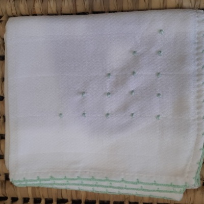 Pano branco com bordado verde sobre superfície de fibra natural entrelaçada