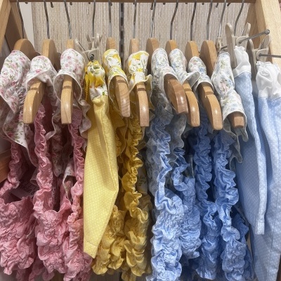 Roupas infantis coloridas penduradas em cabides de madeira com estampado floral e padrão de bolinhas.