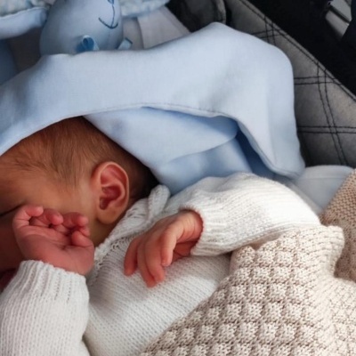 Bebé adormecido com roupa de malha branca e manta bege num carrinho com cobertor azul