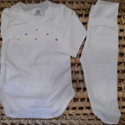 Conjunto de bebé branco com body e calças colocado em superfície de fibras naturais