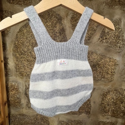 Body de bebé de malha cinza e branco com etiqueta colorida pendurado numa cabide de madeira.