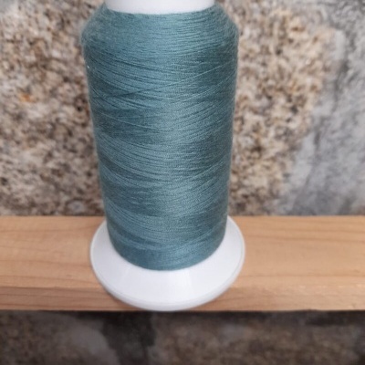 Carretel de linha azul esverdeado num suporte branco sobre madeira clara