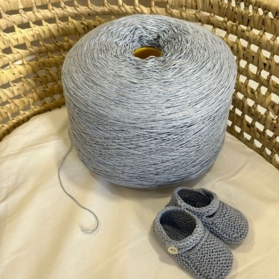 Cone de fio azul claro dentro de cesto de vime com sapatinhos de bebé em fio azul claro