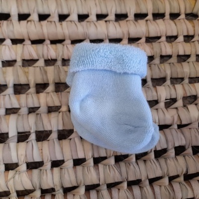 Meia azul clara para bebé colocada sobre superfície trançada bege e castanha