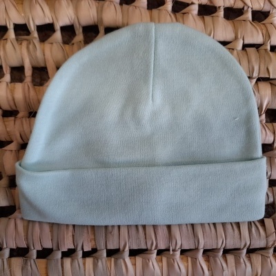 Gorro verde-água sobre superfície entrelaçada bege e castanha