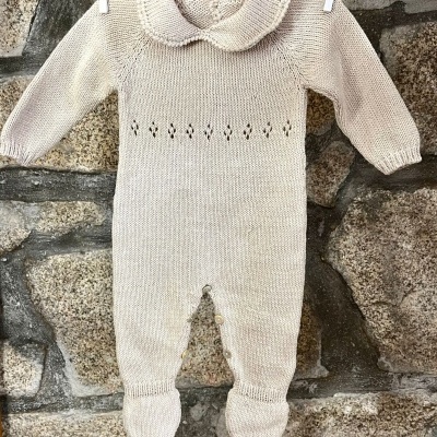 Macacão de bebé em malha bege claro com gola e botões, pendurado numa corda