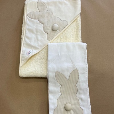 Toalha de banho e toalha de mão creme e branca com aplicação de coelho bege listrado.