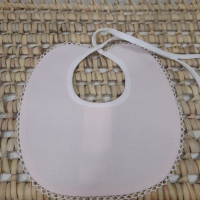 Babete rosa com borda rendada branca sobre tecido trançado bege