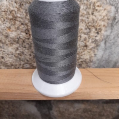 Carretel de linha cinza escuro em suporte branco sobre madeira com parede de pedra ao fundo