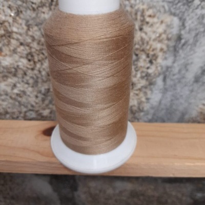 Rolo de linha de costura bege claro num carretel branco sobre madeira