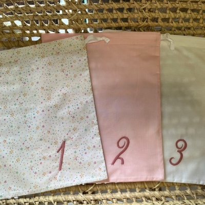 Três sacos de tecido numerados em rosa sobre fundo de vime